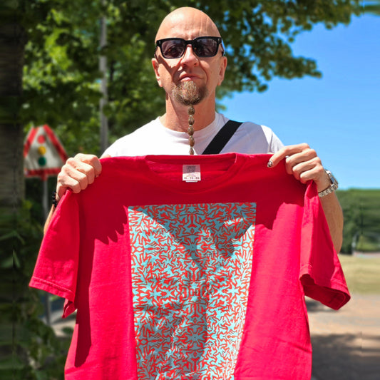 baobabwod. Shavo from System of a Down holding a red BBB t-shirt with a trippy pattern of the Berlin Artist Battern outdoors on a sunny day in Berlin. Designer Fashion for the Streets. 